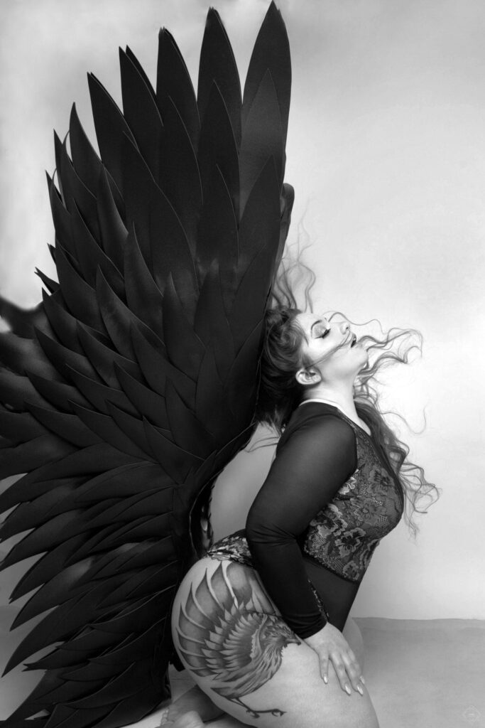 Woman in bodysuit flipping her hair back and wearing XL Black Wings for her Boudoir Session