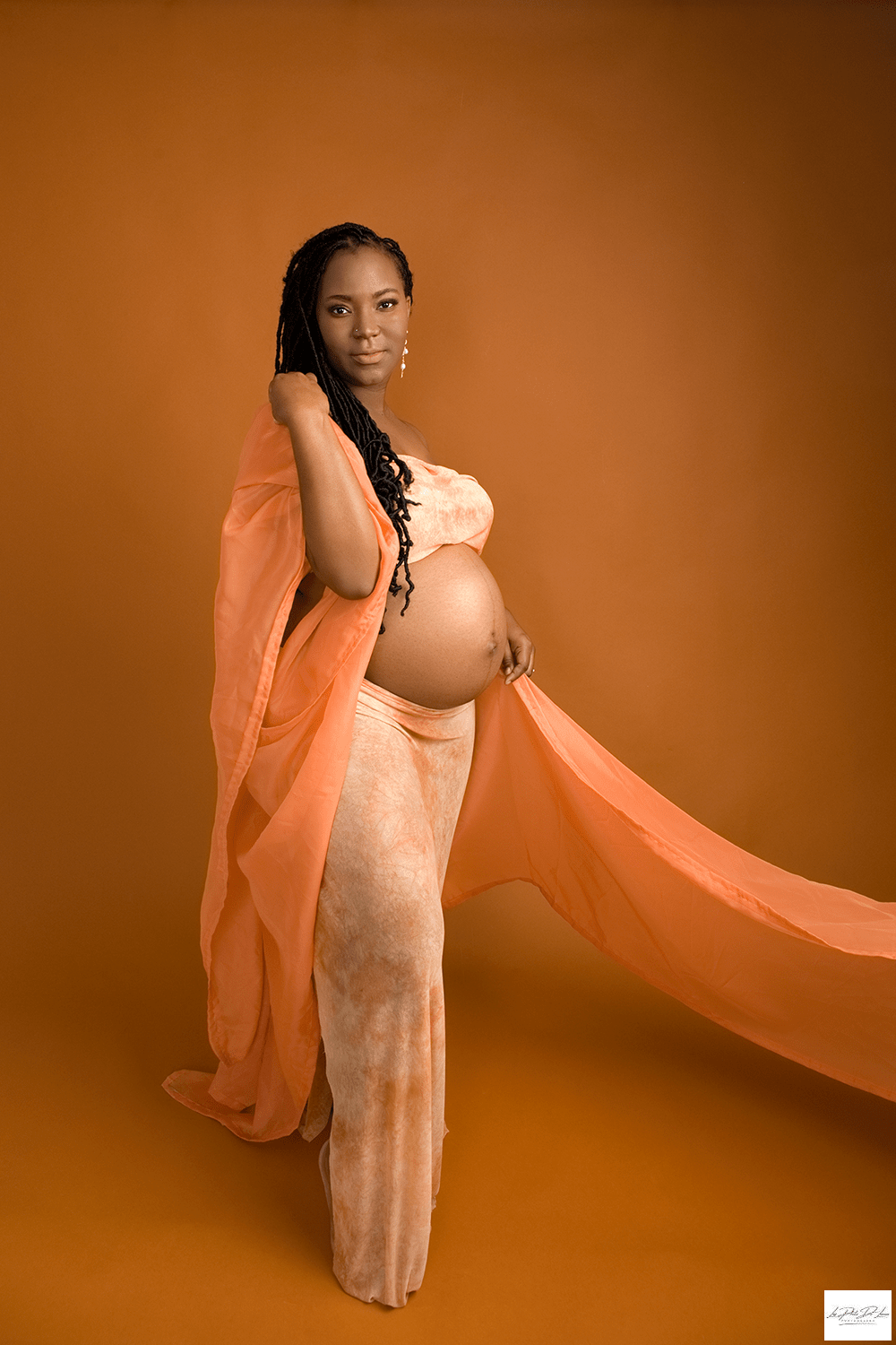 black mom to be dressed in burned orange fabric showing off her baby belly