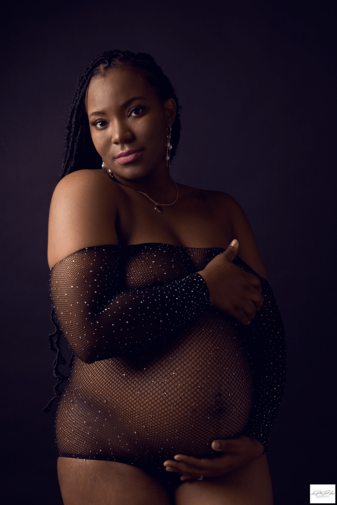 black mom posing for her maternity shoot in a black net body suit with crystals