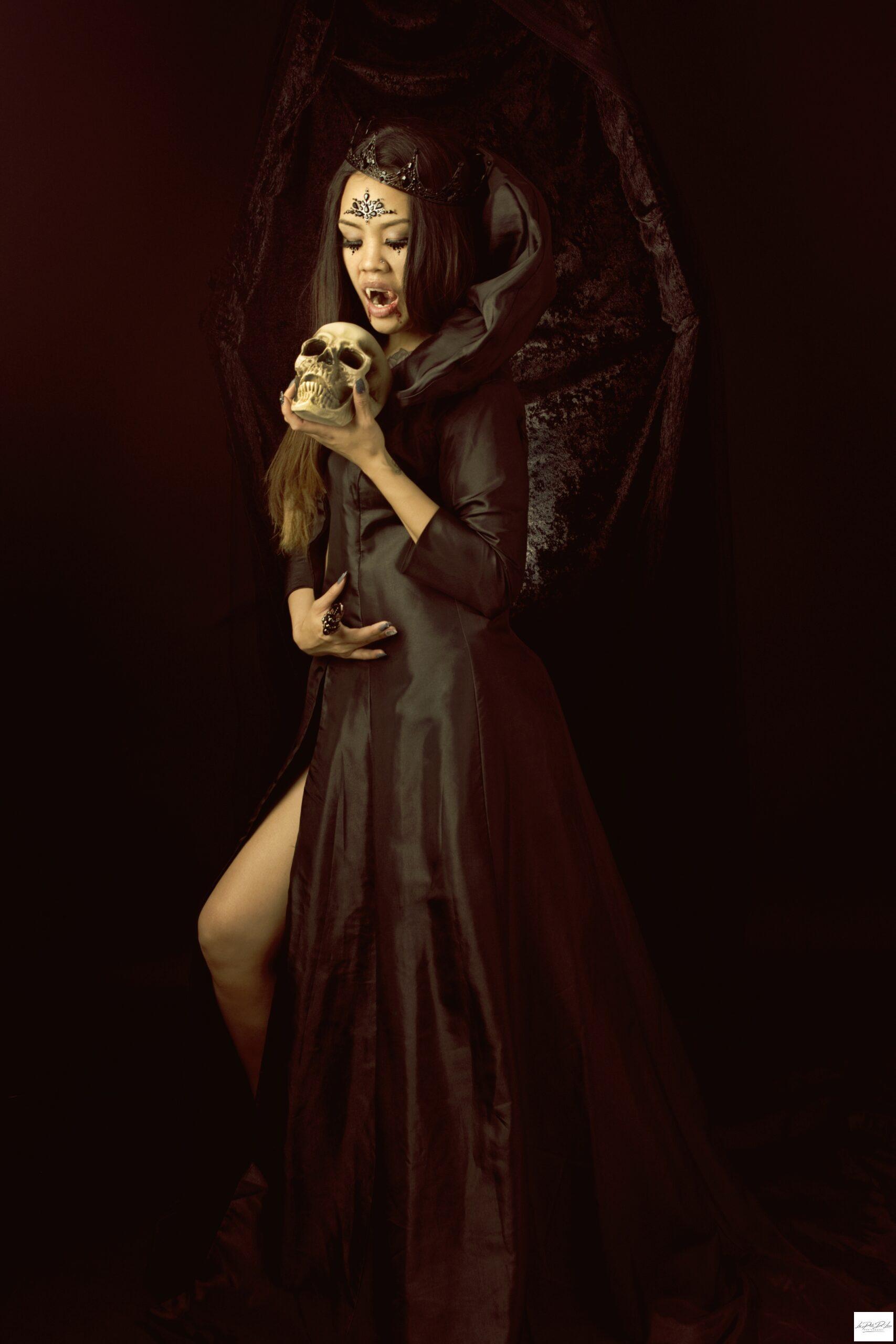 Vampire woman holding a skull posing as the queen of the dark