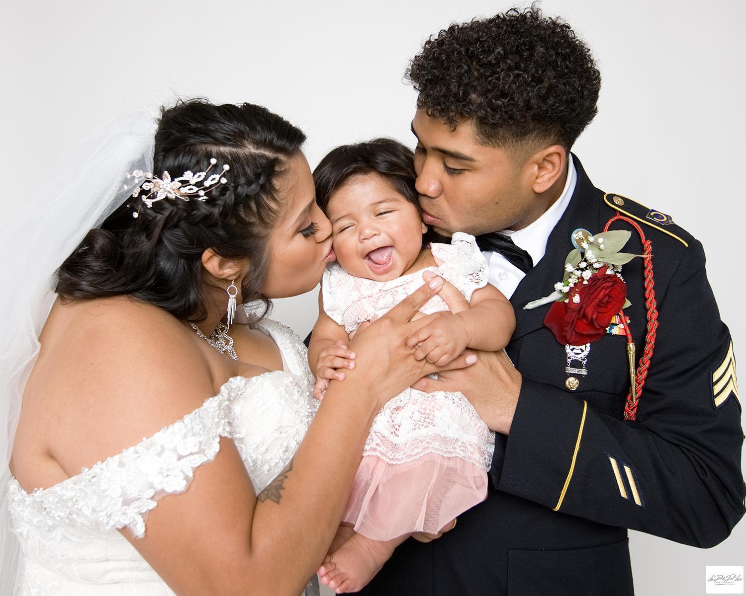 Bride and Groom holding baby girl and kissing her on the cheeks