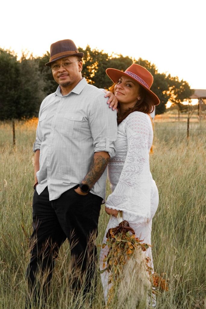 Mixed couple posing in open field with hats and wedding attire