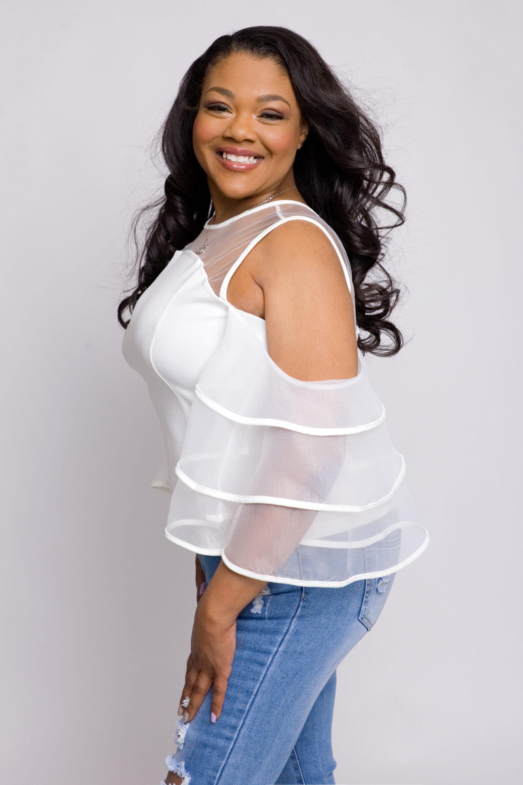 Black woman posing in jeans and white sheer trumpet sleeve blouse while smiling